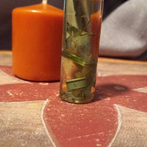 May include: A clear glass bottle filled with a yellow liquid and green plant matter. The bottle has a black lid with the text "BrambleandPateh" on it.