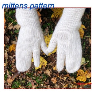 Op de afbeelding: Een paar witte gebreide tabi-wantjes, een traditionele Japanse stijl van wanten met een gescheiden duim, worden getoond tegen een achtergrond van gevallen herfstbladeren.