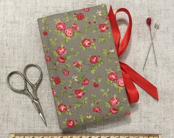May include: A gray fabric sewing kit with a red rose pattern, tied with a red ribbon. Includes silver scissors, two pins, and a wooden ruler with the text "Little Bun Designs UK".