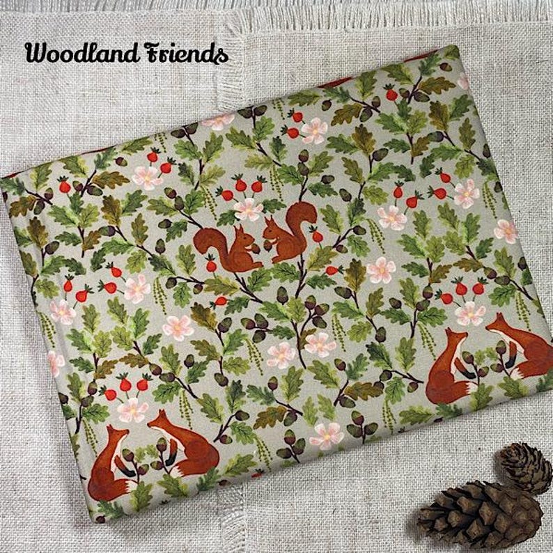 May include: Folded fabric with a woodland design. The pattern features squirrels, berries, and flowers on a light green backdrop. The repeating design includes brown squirrels, red berries, and white flowers. The words "Woodland Friends" are in the upper left corner.