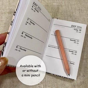 May include: A small, open diary for July 2026, with a small wooden pencil. The diary is open to the week of July 6th, with dates and days of the week visible. The diary has a patterned cover. The text says: Available with or without a mini pencil.