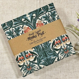 Könnte beinhalten: Ein rechteckiger Notizblock mit einem floralen Muster in Teal, Grün und Orange, umwickelt mit einem braunen Papierband. Auf dem Band steht "Hand Crafted Memo Pad" und "Little Bun Designs UK".