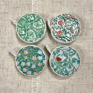 K&ouml;nnte beinhalten: Vier runde, wei&szlig; umrandete, stoffbezogene Ornamente mit floralen Mustern in Gr&uuml;n-, Blau- und Rott&ouml;nen. Die Ornamente haben oben eine Schlaufe zum Aufh&auml;ngen.