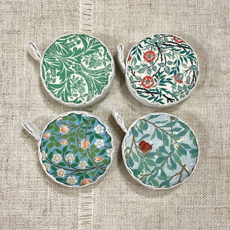 K&ouml;nnte beinhalten: Vier runde, wei&szlig; umrandete, stoffbezogene Ornamente mit floralen Mustern in Gr&uuml;n-, Blau- und Rott&ouml;nen. Die Ornamente haben oben eine Schlaufe zum Aufh&auml;ngen.