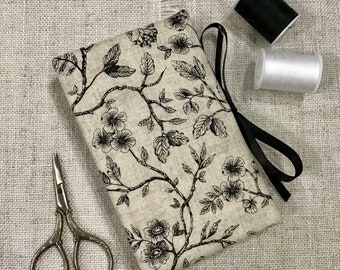 May include: A beige fabric sewing kit with a black floral pattern, a black ribbon, and a pair of small scissors. Two spools of thread, one black and one white, are also present. The kit is designed for sewing and crafting.