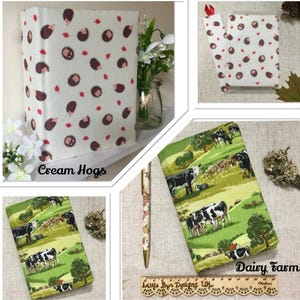 May include: A collection of fabric-covered journals and a pen. One journal features a cream background with brown hedgehogs and red leaves. Another journal displays a green landscape with cows. The text "Cream Hogs" and "Daisy Farm" are visible.