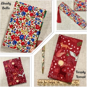 Op de afbeelding: Een stoffen boekomslag met bloemenpatroon gelabeld Liberty Belle, een bijpassende bladwijzer met rode kwast en een stoffen boekomslag met bosdierenprint gelabeld Frosty Forest, vergezeld door een bijpassende pen en liniaal.