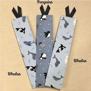 Op de afbeelding: Drie rechthoekige stoffen boekenleggers met zwart-witte stippenlintjes. De buitenste twee hebben een lichtblauwe achtergrond met walvisillustraties en de tekst Whales. De middelste is grijs met pingu&iuml;nafbeeldingen en de tekst Penguins.