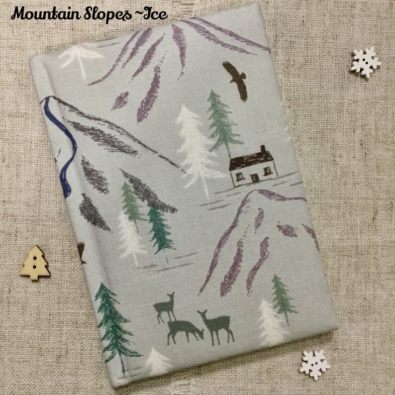 May include: A gray fabric notebook with a wintery mountain scene design. The design features a small house, trees, deer, and a bird flying over the mountains. The text "Mountain Slopes - Ice" is printed on the front cover.