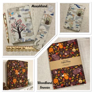 Op de afbeelding: Twee met stof beklede dagboeken en een bijpassende bladwijzer. E&eacute;n dagboek heeft een moerasprint met een boom, vogel en stenen. De andere, met het label Woodland Snooze, heeft een donkerbruine achtergrond met vossen, egels en herfstbladeren.