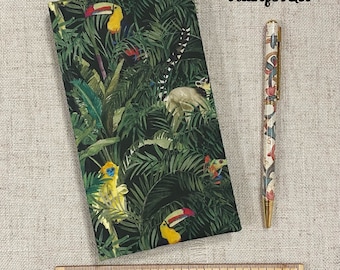 Op de afbeelding: Een notitieboek en pennen set met een regenwoud thema. Het notitieboek heeft een donkergroene kaft met toekans, apen en weelderig gebladerte. De pen heeft een witte schacht met een bloemenpatroon en gouden details.