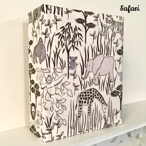 May include: A white fabric with a black and brown safari animal print. The print includes a giraffe, elephant, monkey, gorilla, and tiger. The fabric has the word "Safari" printed in the top right corner.