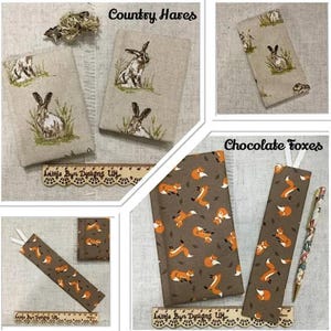 May include: A collection of fabric-covered notebooks and bookmarks. Some feature embroidered hares in a field, while others display a pattern of orange foxes on a brown background. The text "Country Hares" and "Chocolate Foxes" are visible.
