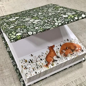 Peut inclure: Un bloc-notes recouvert d'un tissu floral vert avec un intérieur blanc et une illustration de renard sur le devant. Le bloc-notes a une fermeture magnétique et est parfait pour noter des notes, des idées ou des listes.