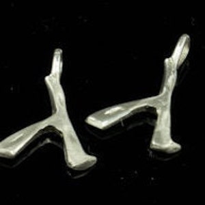 Puede incluir: Dos abalorios de plata con forma de hacha estilizada, cada uno con un bucle para sujetar a un collar o pulsera.