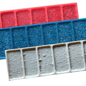 May include: Three concrete stamp pads in red, blue, and gray. Each pad has a textured surface with a pattern of rectangular shapes.