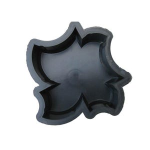 May include: Black rubber mold for making concrete stepping stones. The mold is shaped like a stylized flower with four petals.