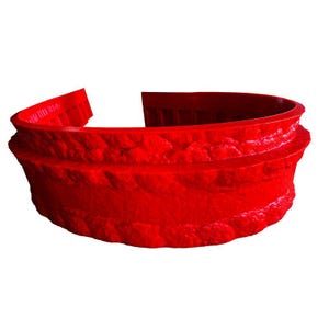 May include: A vibrant red, semi-circular decorative object with a textured, stone-like appearance. The object has a layered design and a smooth, curved interior. The open ends suggest it could be a planter or decorative border.