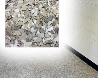 May include: A collection of decorative floor flakes in shades of beige, white, and gray, shown in a square inset above a finished floor surface that features a speckled, multi-colored texture applied to a concrete floor next to a white wall.