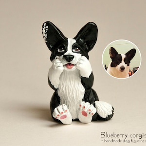May include: A black and white hand-painted ceramic figurine of a Cardigan Welsh Corgi dog. The dog is sitting with its paws covering its face and has a pink nose and tongue. The figurine is a custom portrait of a real dog.