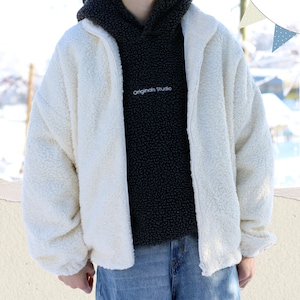 May include: A white sherpa jacket with a zipper closure. The jacket is worn over a black hoodie with the text "Originals Studio" embroidered on the front.