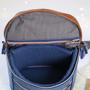 K&ouml;nnte beinhalten: Eine blaue Jeans- und braune Leder-Umh&auml;ngetasche mit Rei&szlig;verschluss und einem wei&szlig;en Etikett mit der Aufschrift "Blah Blah Blah".