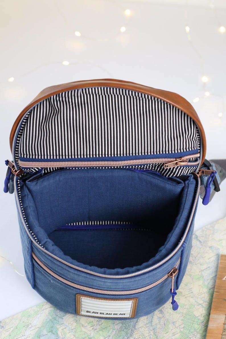 K&ouml;nnte beinhalten: Eine blaue Jeans- und braune Leder-Umh&auml;ngetasche mit Rei&szlig;verschluss und einem wei&szlig;en Etikett mit der Aufschrift "Blah Blah Blah".
