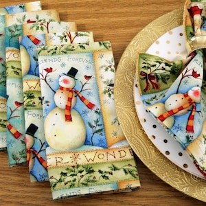 May include: Set of six blue and green fabric napkins with a snowman and winter scene design. The napkins feature the text "Friends Forever" and "Winter Wonderland".