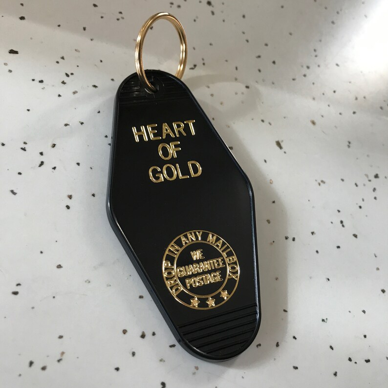 May include: Black motel key chain with gold lettering that reads "Heart of Gold" and a gold circle with the text "Drop in any mailbox, We Guarantee Postage".