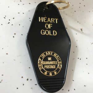 May include: Black motel key tag with gold lettering that reads "HEART OF GOLD" and a gold circle with the text "DROP IN ANY MAILBOX WE GUARANTEE POSTAGE" and three gold stars.