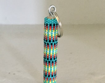 May include: A beaded keychain with a turquoise, black, red, yellow, and white geometric pattern. The keychain is attached to a silver key ring.