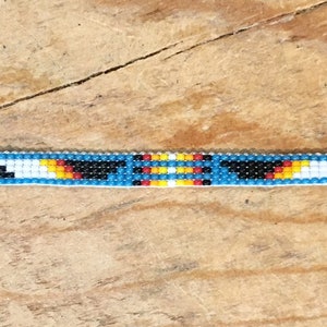 May include: A beaded bracelet with a blue background and geometric patterns in black, white, yellow, and red.