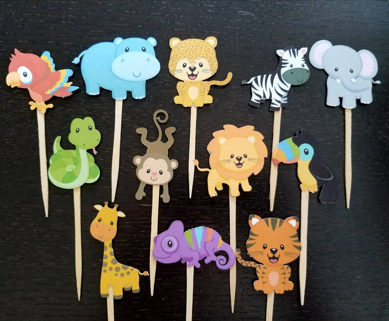 May include: A set of 12 colourful animal cupcake toppers, featuring a variety of jungle animals, including a lion, giraffe, toucan, hippopotamus, monkey, and more. The toppers are perfect for a jungle-themed party.
