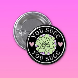 May include: Black and white button with a green succulent plant and the text "You Succ You Succ" in a circle. There are two pink hearts on either side of the text.