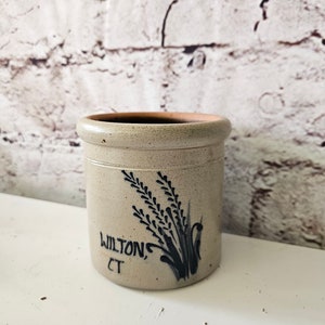 Puede incluir: Un tarro de cerámica de color crema con un diseño azul y negro de tallos de trigo y el texto "WILTON, CT".