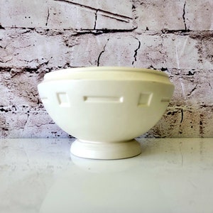 May include: A white ceramic bowl with a geometric design around the rim. The bowl has a pedestal base.