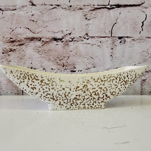 May include: A white ceramic planter with a speckled gold glaze. The planter is shaped like a boat and has a wide, shallow base.