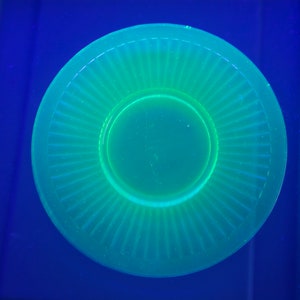 May include: A bright green glass saucer with a fluted edge and a smooth, circular center. The saucer is a vibrant shade of green and appears to be made of uranium glass.