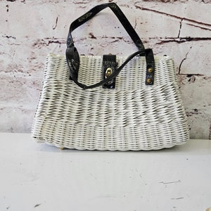 Pode incluir: Bolsa de vime branca com alças de couro preto e fecho dourado. A bolsa tem um padrão tecido e é acentuada com tachas de metal preto.