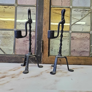 May include: Two black metal candle holders with a twisted design and three legs. The candle holders are made of wrought iron and have a rustic look.