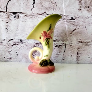 May include: A small, white ceramic vase with a green and pink floral design. The vase is shaped like a horn and has a handle.