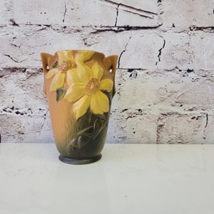 May include: A brown and yellow ceramic vase with a floral design. The vase has two handles and a textured surface.