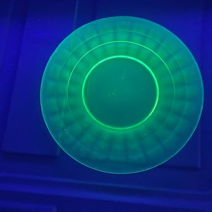 May include: A green glass plate with a concentric circle design. The plate is illuminated with a black light, causing it to glow.