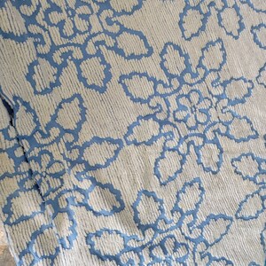 May include: A white throw blanket with a blue floral pattern. The blanket has a textured, fluffy surface and a fringe border.