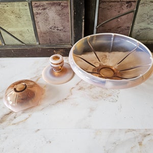 May include: Three vintage glass pieces in a pastel pink and amber colour. A small bowl, a small lidded dish, and a candle holder.