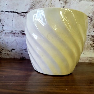 Peut inclure: Un pot en céramique blanc avec un motif en spirale. Le pot a un glaçage jaune clair.