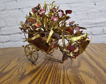 Op de afbeelding: Een gouden en rode metalen sculptuur van een koets met een groot boeket bloemen. De sculptuur is gemaakt van draad en metaal en heeft een rustieke, vintage uitstraling.