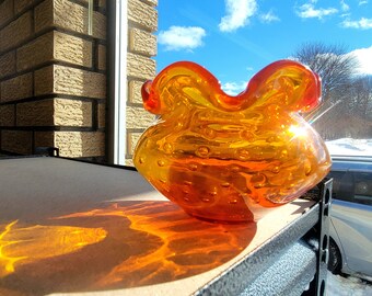 May include: A large, orange glass bowl with a textured, bubbled surface. The bowl has a ruffled edge and is sitting on a shelf.