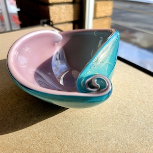 May include: A small, teal and pink glass bowl with a swirl design. The bowl is made of glass and has a shiny finish.