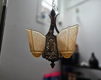 May include: A vintage brass chandelier with three frosted glass shades. The shades have a geometric pattern and are attached to a decorative metal frame.